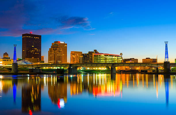 Dayton Downtown Skyline with River at Dusk Downtown Dayton skyline with the Miami River and skyline reflections at dusk. dayton ohio skyline stock pictures, royalty-free photos & images