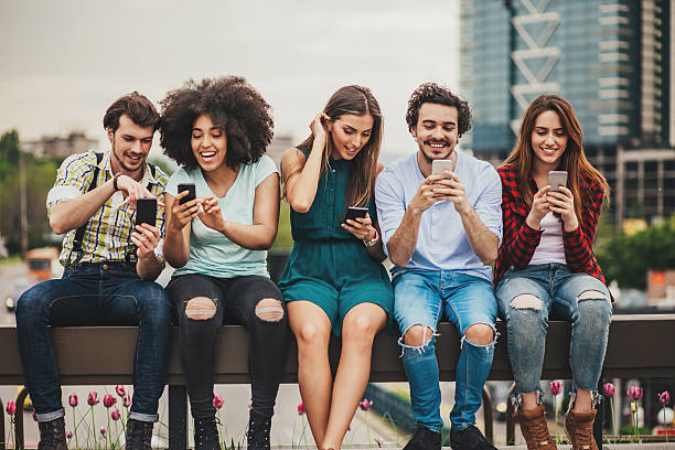 Connecting and sharing Multi-ethnic group of people sitting on an urban bridge text messaging and sharing smart phone content. five people photos stock pictures, royalty-free photos & images
