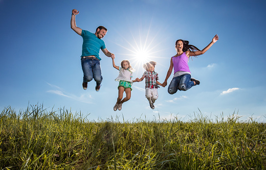 Playful family having fun in nature and jumping high up against the sky. Copy space.