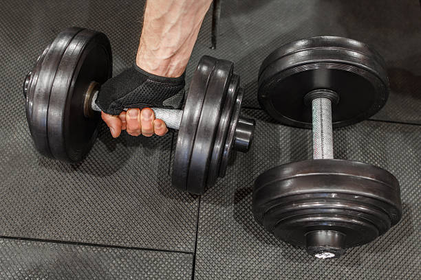 istock Two dumbbells on gym floor, one held by mans hand 543088166