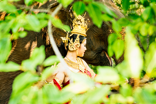 Tradtionally dressed Thai model with an elephant seen through the jungle.