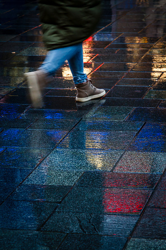 Girl walking in the reflection of neon lights on the wet sidewalk.