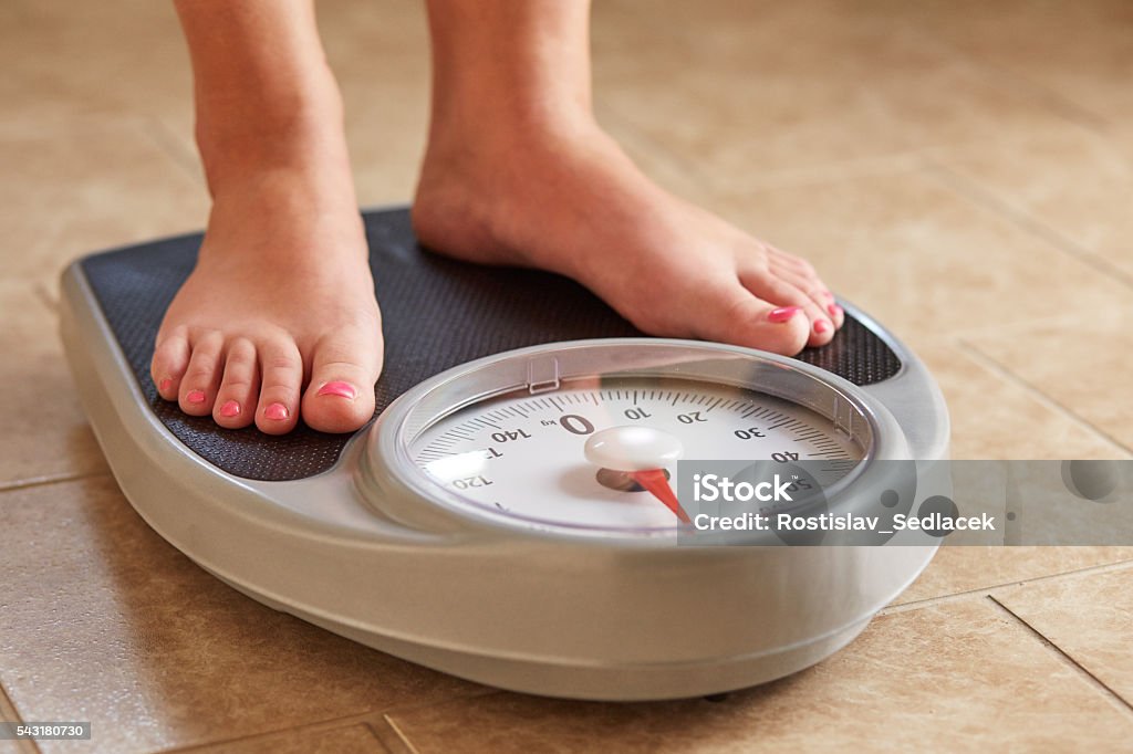 Female feet on weight scale A pair of female feet on a bathroom scale Weight Scale Stock Photo