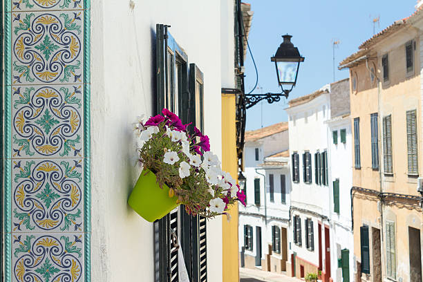 Decorative tiles and flowers in small street at Alaior, Menorca Close up of tiles with floral pattern and a flowerpot in a small city alley. minorca photos stock pictures, royalty-free photos & images