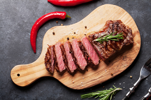 Grilled sliced beef steak on cutting board over stone table. Top view