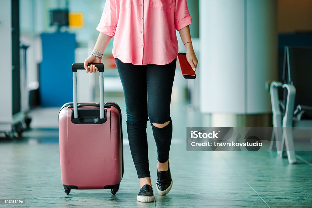 Passenger with passports and boarding pass and pink baggage Closeup airplane passenger with passports and boarding pass and pink baggage in an airport lounge. Young woman in international airport walking with her luggage. Airport Stock Photo