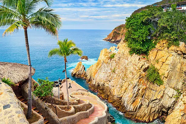 Photo of the landmark La Quebrada diving cliffs and waterfront promenade in Acapulco, Mexico.  La Quebrada is famous for the divers that entertain tourists by jumping off the cliff.