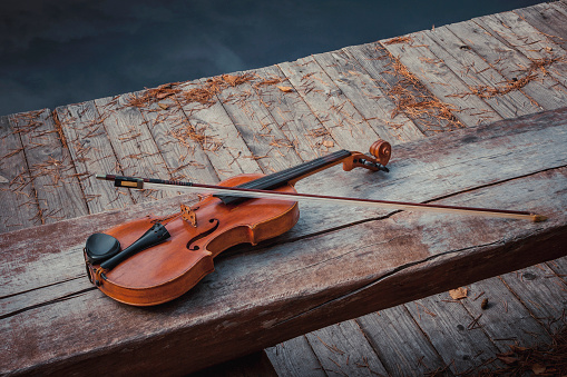 Old violin with a bow lies on a wooden bench