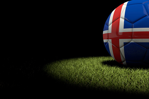 A 3D render of a soccer football ball on a grass sports pitch. The ball is lit by a dramatic circle spotlight with the rest of the image in black darkness.