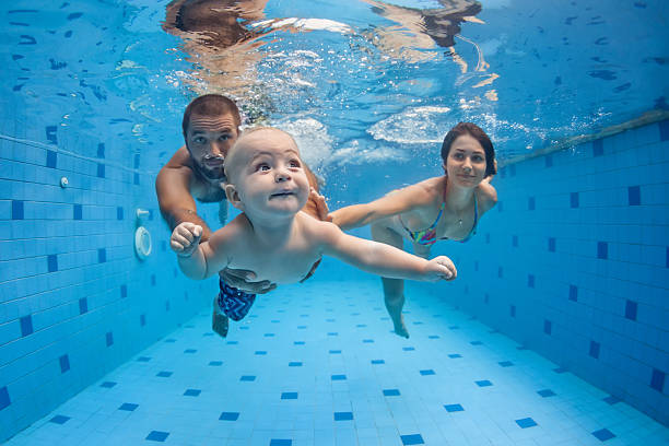 Happy full family swim and dive underwater in swimming pool Happy full family - mother, father, baby son learn to swim, dive underwater with fun in pool to keep fit. Healthy lifestyle, active parent, people water sport activity, swimming lesson. Focus on child loon bird stock pictures, royalty-free photos & images