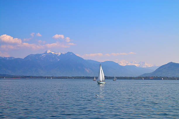 The photo was taken in Germany, at Lake Chiemsee. The picture shows a walk on a yacht on mountain lake. In the background snowy mountains visible.