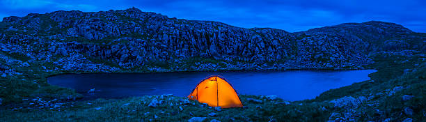 Orange dome tent camping beside remote mountain lake wilderness panorama