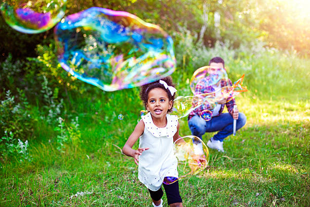 pai e filha felizes brincando com bolhas de sabão no parque. - bubble wand bubble child playful - fotografias e filmes do acervo