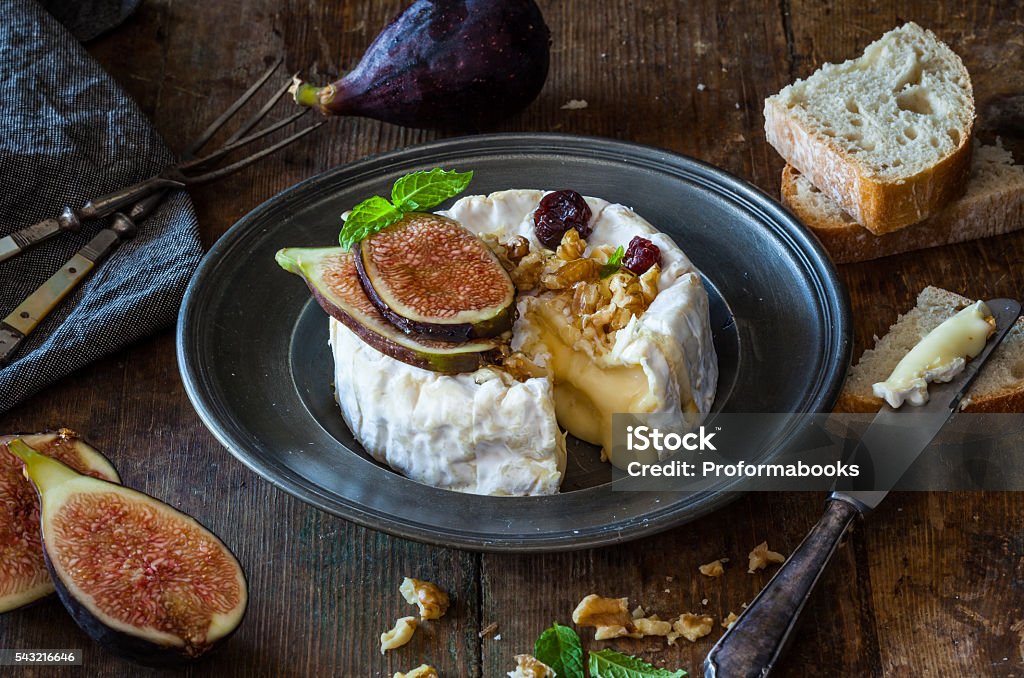 camembert Camembert cheese with fresh figs, honey, walnuts and raisins on a rustic vintage wooden table. Dark and moody. French Food Stock Photo