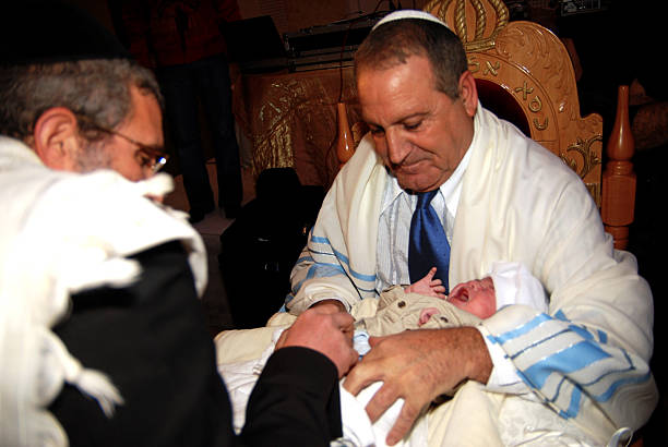 Brit Milah and Circumcision Ceremony Jerusalem, Israel - January 1, 2008: Grandfather holds his grandchild while he is circumcised by a Jewish Mohel (Person trained in the practice of Brit Milah) in Jerusalem, Israel. It's a religious ceremony within Judaism to welcome infant Jewish boys into a covenant between God and the Children of Israel. circumcision surgery stock pictures, royalty-free photos & images