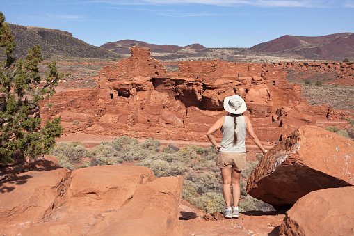 With the volcanic hills in the background, a young woman with a pony tail admires the view from the trail overlooking Wupatki Pueblo ruins in Wupatki National Monument at Flagstaff, Arizona.