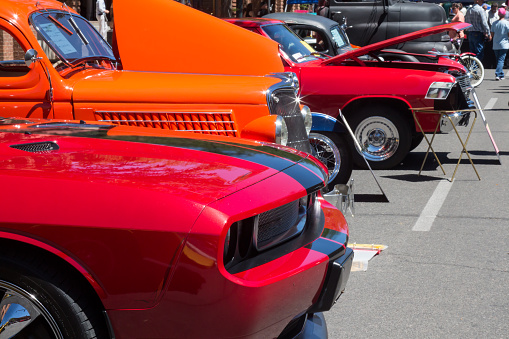 Durango, Colorado, USA - June 18, 2016: Red and orange cars at a car show, lined up on the street.  The cars are muscle and vintage cars.  Some of the cars have their hoods raised.  The paint jobs on the cars are pristine, clean and shiny.
