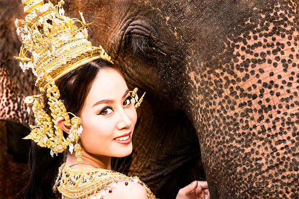 Thai Model and Elephant Close Up Tradtionally dressed Thai model close up with an elephant. thai traditional costume stock pictures, royalty-free photos & images