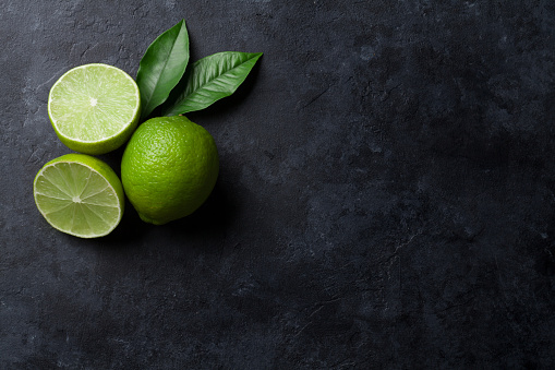 Fresh ripe limes on dark stone background. Top view with copy space