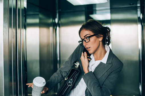Young woman in business wear talking on the phone and catching the elavator