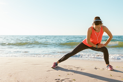 Slim athletic girl in a red t-shirt has been stretching in the morning on the beach in the sunshine. Concept sports lifestyle, space for text.