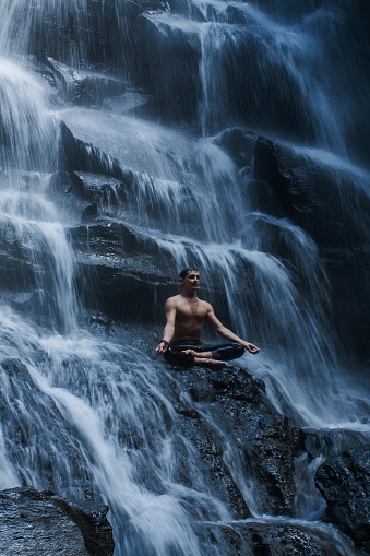 Young man in a yoga pose at the waterfall