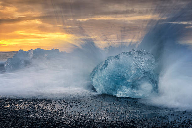 Waves splasing on a washed up iceberg block at the black volcanic beach near the Jokulsarlong ice lake in Iceland during sunrise.