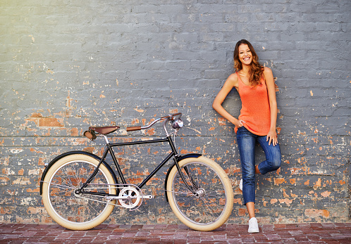 Shot of a young woman posing with her bicycle against a grey background