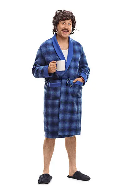 Full length portrait of a relaxed man in blue bathrobe holding a cup of coffee isolated on white background