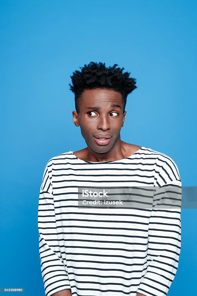 Portrait of surprised afro american guy Portrait of surprised afro american young man wearing striped top, looking away. Studio portrait, blue background. Rolling Eyes Stock Photo