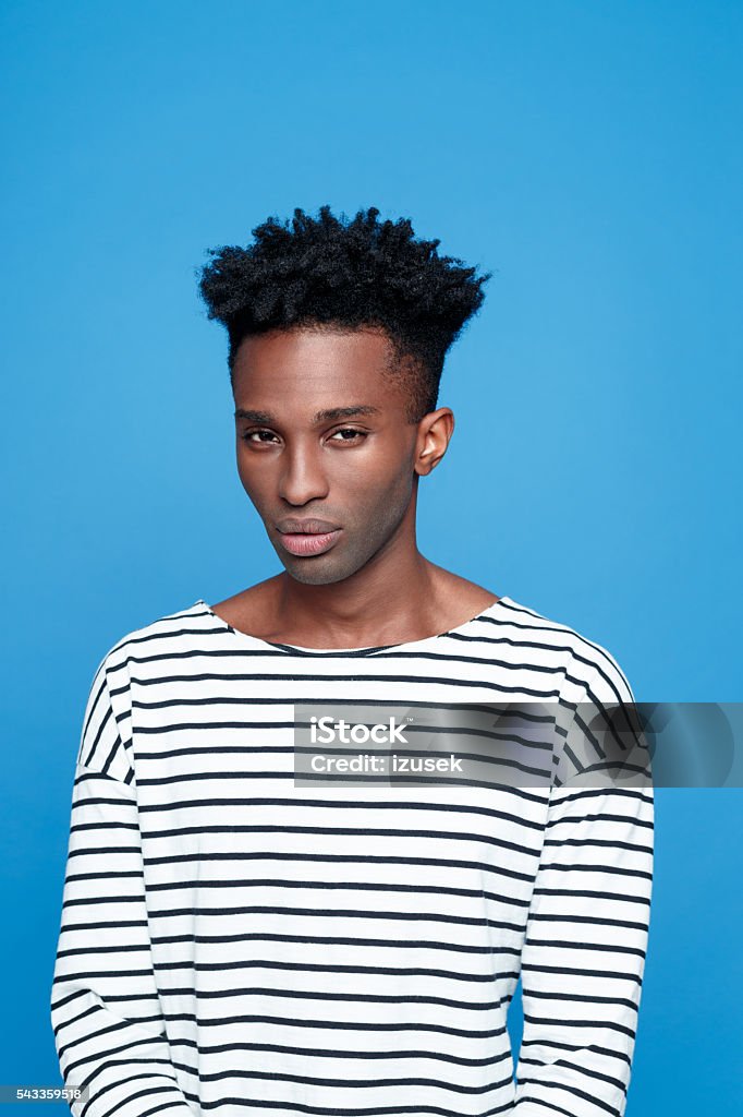 Portrait of serious afro american guy Portrait of serious afro american young man wearing striped top, looking at camera. Studio portrait, blue background. Adult Stock Photo