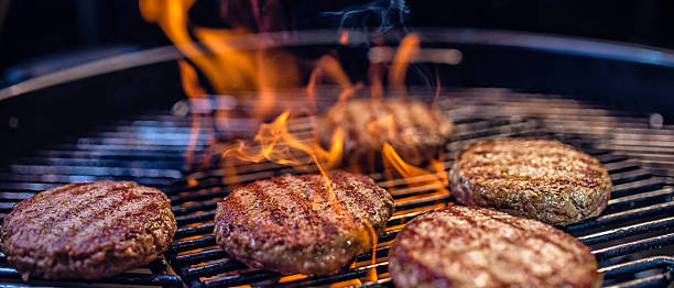 Close-up of meat patties on a barbecue Close-up of juicy burger patties on a ribbed barbecue, flames enveloping the meat. grill burgers stock pictures, royalty-free photos & images