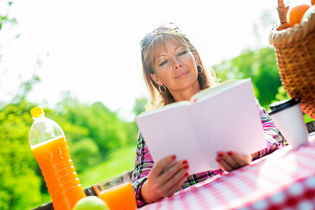 Beautiful mature woman.Happy woman reading a book during springtime in the park.
