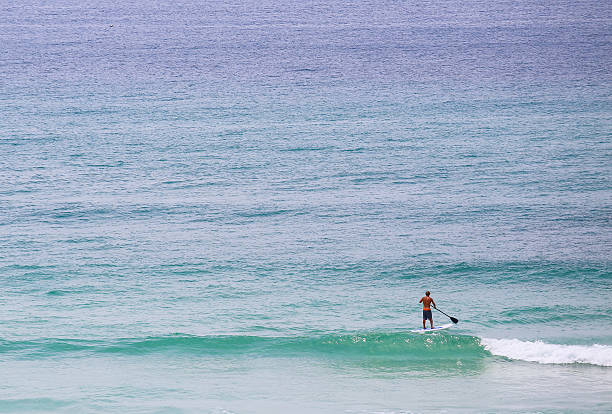 Pensacola Beach, United States - May 13, 2015: A man doing standup paddleboarding in light surf close to the beach.