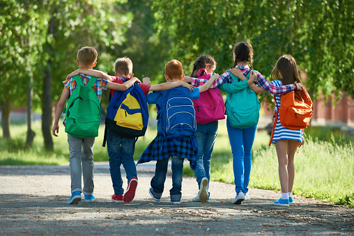 Group of classmates with school bags embracing each other and walking