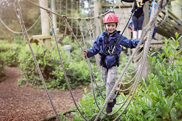 Boy in a harness on a treetop adventure park walking across a rope bridge