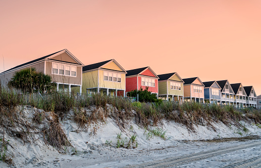 A summer scene on the beach with cottages in a line.