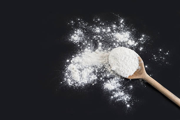 Wooden spoon with flour against isolated on black background stock photo