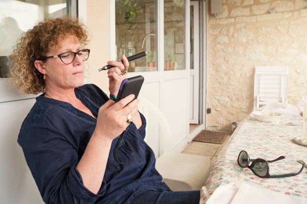 Mature woman smoking e-cigarette while looking at mobile phone.