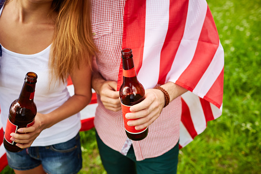 Friendship. Close-up of couple holding beer bottles. Two people drinking alcohol beverage. They covered with usa flag. It is perfect for using it in commercial and advertising photography, reports, books, presentation