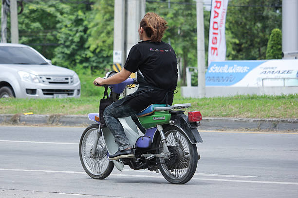 Asian female bike taxi driver wearing helmet sitting on her moped outdoors