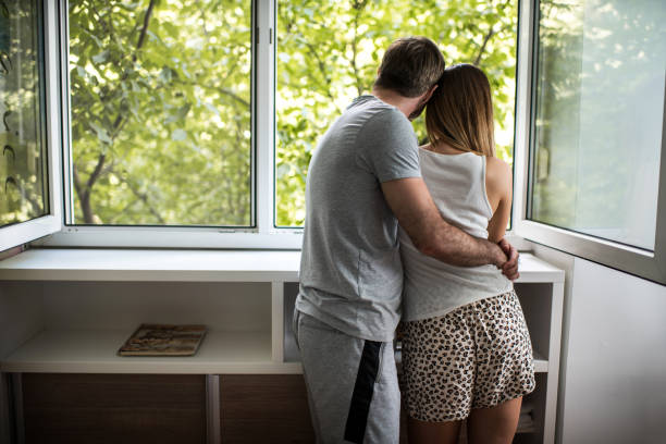 istock Back view of embraced couple looking through the window. 543557680
