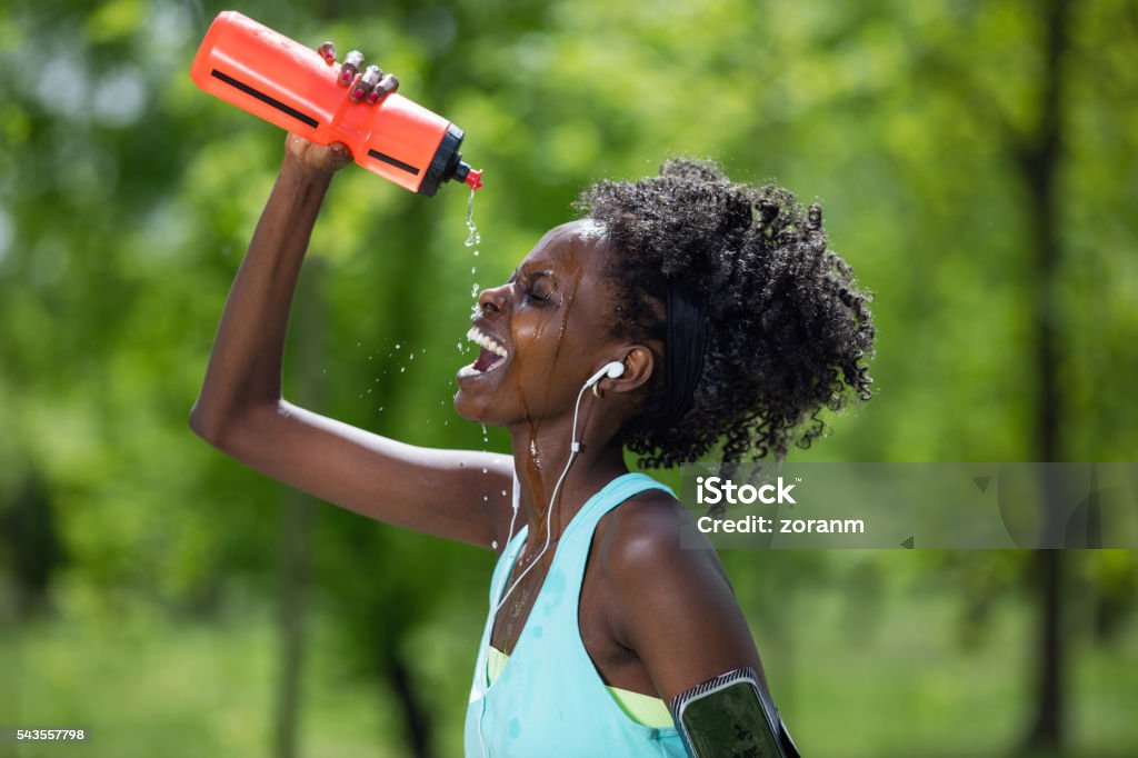 Tired female runner cooling down Tired black female jogger pouring water on her head Pouring Stock Photo