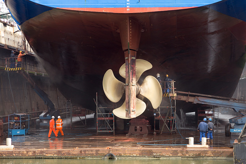 Rotterdam, The Netherlands - September 5, 2015: Workers removing algue from the underside of a ship in a repair dry dock.