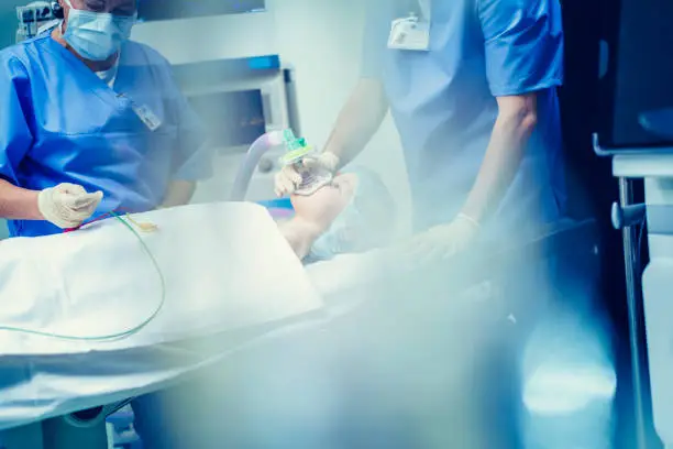 Blurred shot of a young boy with oxygen mask lying on bed surrounded with doctor's team in operating room.