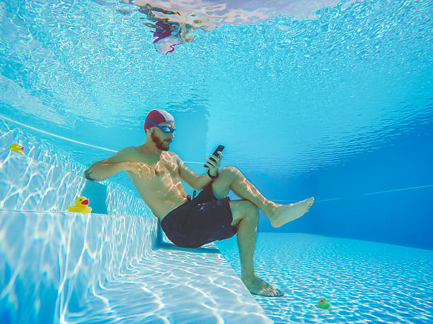 Addicted to social networking: with mobile phone underwater Workaholic man underwater, social networking on the mobile phone. He is surrounded by small yellow plastic ducks underwater diving photos stock pictures, royalty-free photos & images
