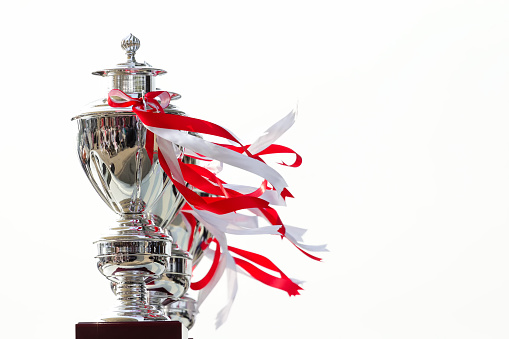 Row of cup trophy tied with white and red ribbon on white background, award for winner or champion, with copy space.