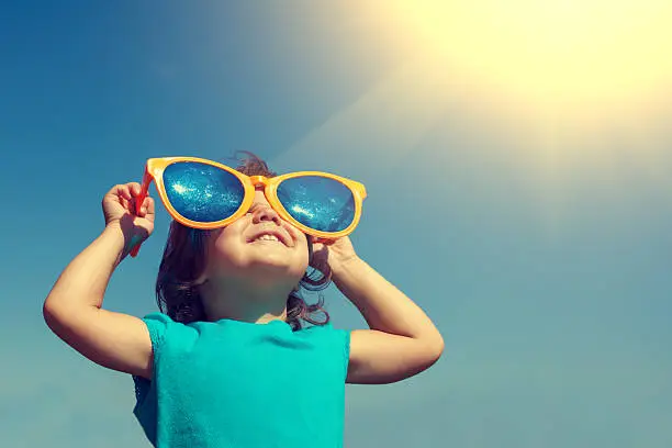Photo of Happy little girl with big sunglasses looking at the sun