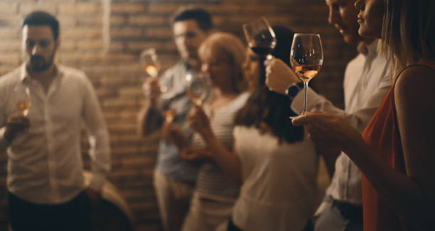 Wine tasting in a wine cellar. Closeup side veiw of group of adults during wine tasting in a wine cellar. There are three women and three men tasting different kinds of wines, selective focus. Low key. wine tasting stock pictures, royalty-free photos & images