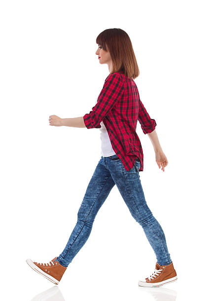 Walking Casual Girl Side View Woman in red lumberjack shirt, jeans and brown sneakers walking and looking away. Side view. Full length studio shot isolated on white. legs apart stock pictures, royalty-free photos & images